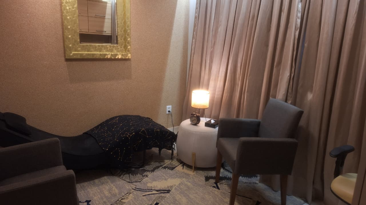 Poltrona ao lado da luminária acesa e do divã, com cortinas ao fundo